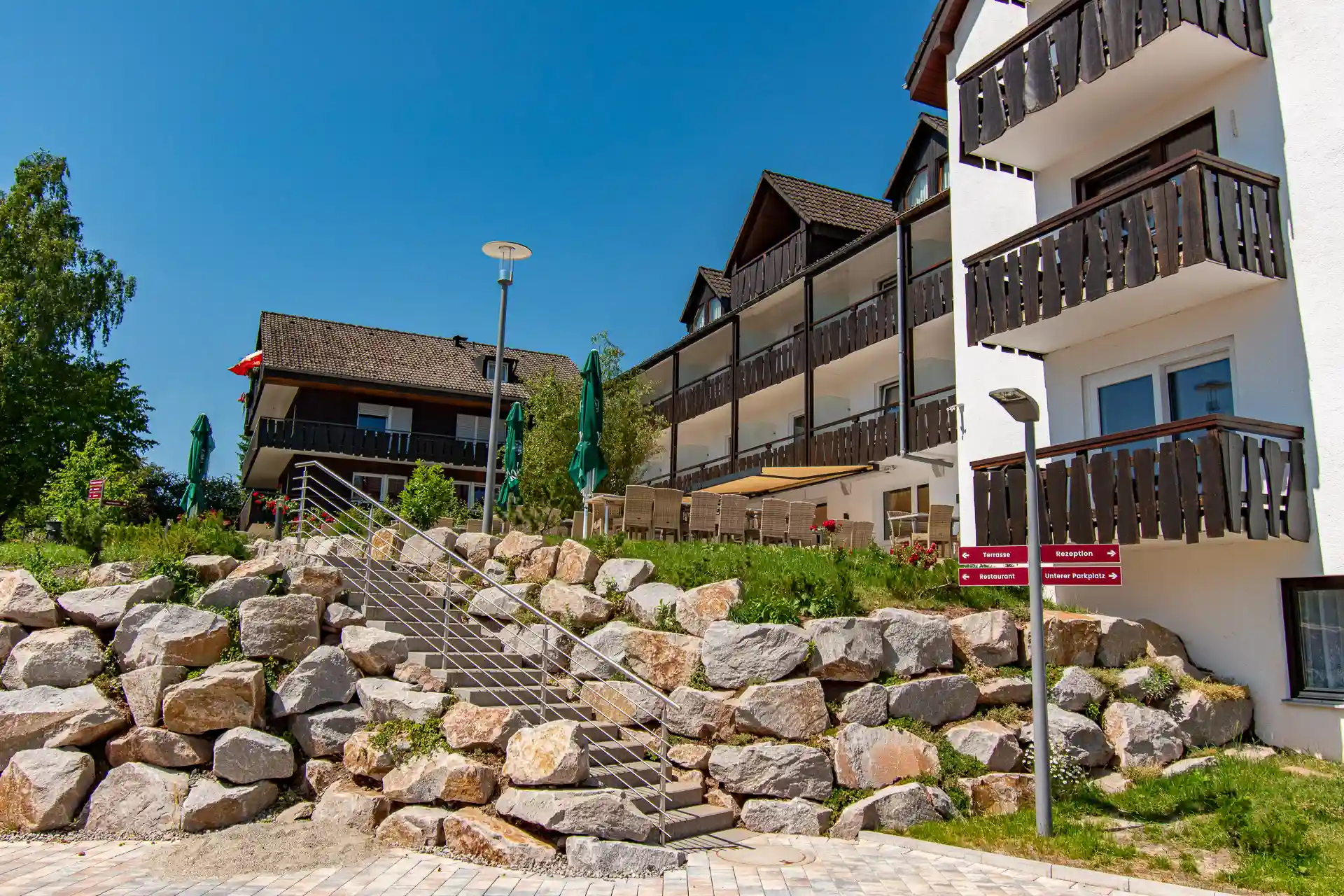 Exterior view of the Wellnesshotel Hohenrodt with the hotel building, a parking lot and the inviting staircase leading to the entrance