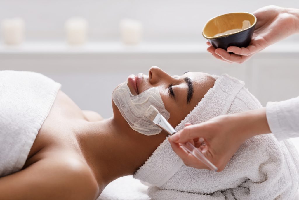 Beautician applies a clay face mask to a woman's face