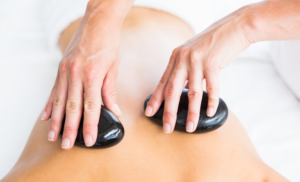 Masseur führt eine Hot-Stone-Massage am Rücken einer Frau im Spa durch