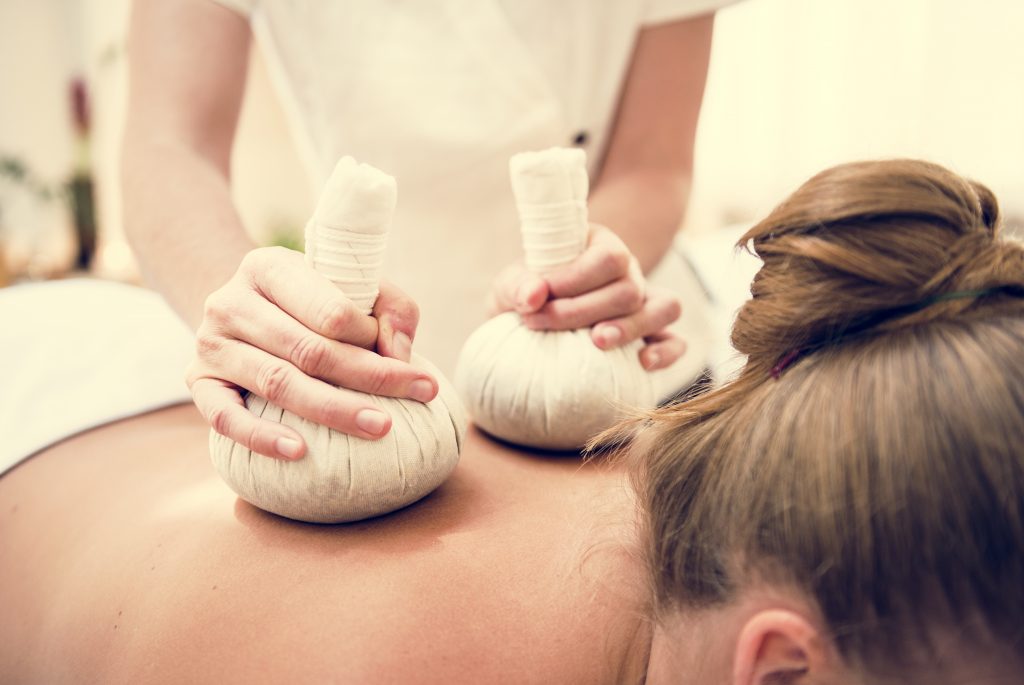 Kräuterstempel-Massage mit einem Tuch, das mit Heilkräutern gefüllt ist, für eine entspannende und therapeutische Behandlung