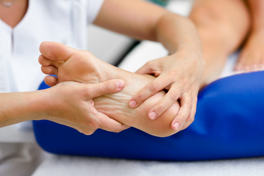 Weibliche Masseurin untersucht ihre Patientin für eine medizinische Fußmassage