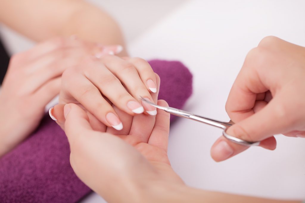 Close-up of a woman in a nail salon receiving a manicure with scissors from a beautician