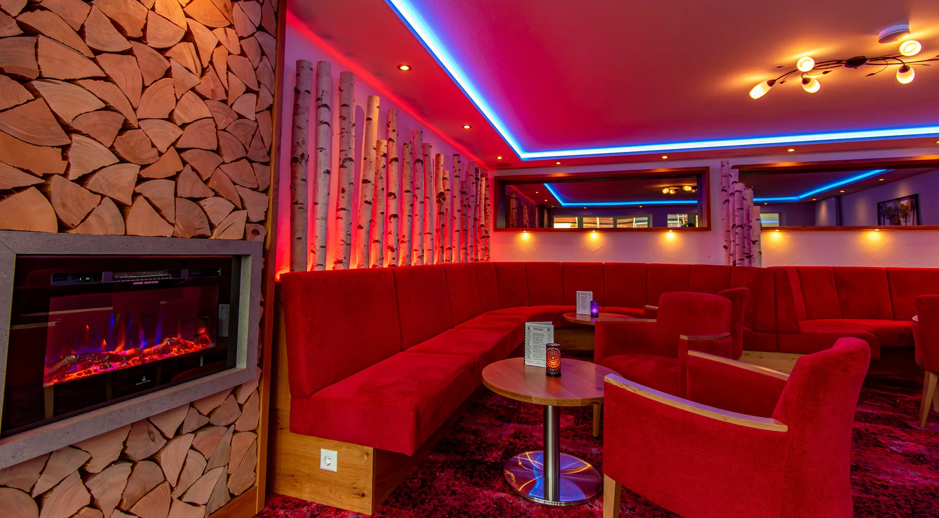 Wellnesshotel Hohenrodt, Rezeption und Lounge mit Kamin und Birkenstämmen für eine warme, einladende Atmosphäre