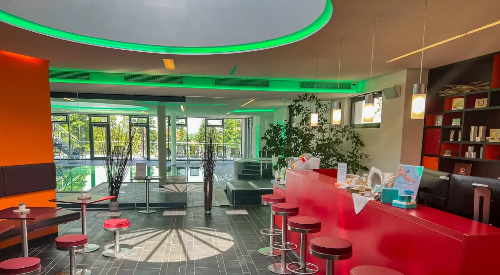 Stimmungsvolle Wellness-Rezeption mit grüner LED-Beleuchtung und stilvollem Blick auf den angrenzenden Poolbereich