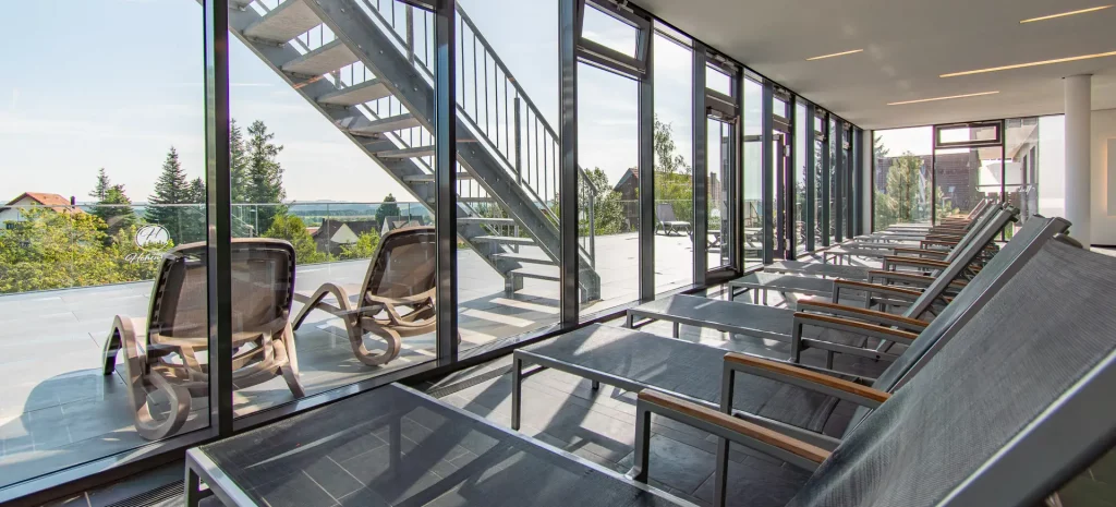 Wellness pool area at Wellnesshotel Hohenrodt with loungers, large window front, and a view of the landscape
