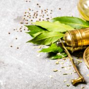Antike Ayurveda-Mühle mit duftenden Gewürzen und Lorbeerblättern auf steinernem Tisch