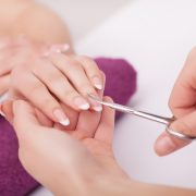 Nahaufnahme einer Frau im Nagelstudio, die von einer Kosmetikerin eine Maniküre erhält, bei der eine Schere verwendet wird