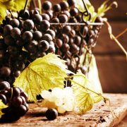 Grapes with leaves in a metal basket on a rustic wooden table, close-up.